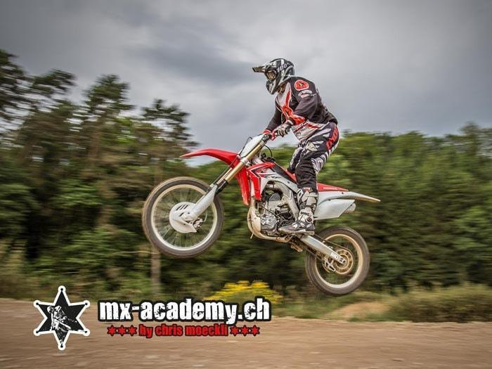 BMX und Motocross: Fahrer springt mit seinem Motocross-Bike über eine Kuppe vor Bäumen