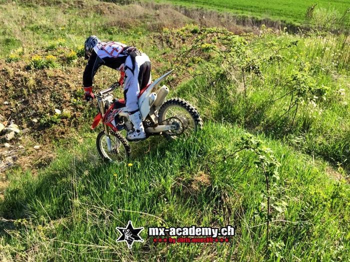Fahrer lenkt sein Motorrad über Wurzeln und Gras einen Hang hinauf, ähnlich wie im Trial