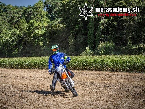 Auszeit nehmen im Grünen: Fahrer in blauer Jacke auf orangem Motorrad neben einem Maisfeld