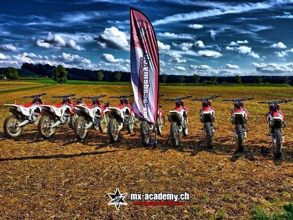 Honda-Motorräder stehen in einer Reihe neben der MX-Academy-Fahne unter Wolken – bereit für die nächsten Motocross Termine