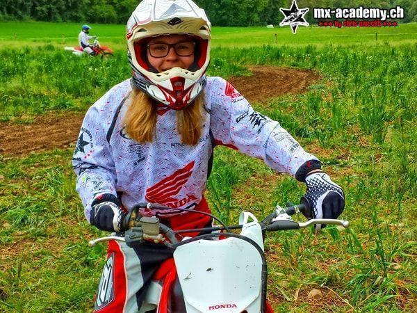 Lächelnde Fahrerin mit Brille und weissem Helm sitzt auf einer Honda im Grünen – Motorrad ausprobieren als Frau