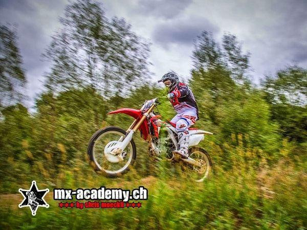Dirt Bike im Sprung: Ein Fahrer fliegt auf seiner roten Honda über die Wiese, leicht verwischt
