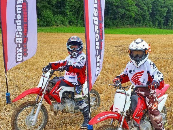 Zwei Kinder auf Honda-Kindermotorrädern zwischen zwei MX-Academy-Fahnen – Kinder Cross in der Gruppe