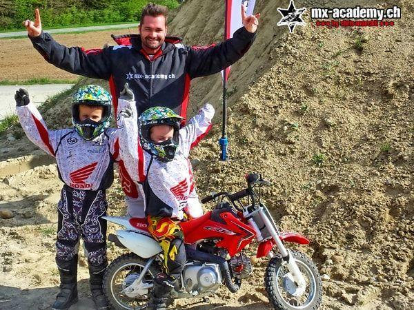 Zwei Kinder in Honda-Bekleidung jubeln am Kindermotorrad, im Hintergrund ein Erwachsener – Gutschein Motocross für Kinder