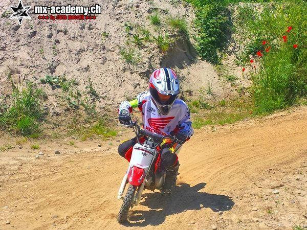 Kind auf einem Honda-Kindermotorrad auf dem Sandweg, daneben blüht roter Mohn – Kindercross Motorrad von Honda