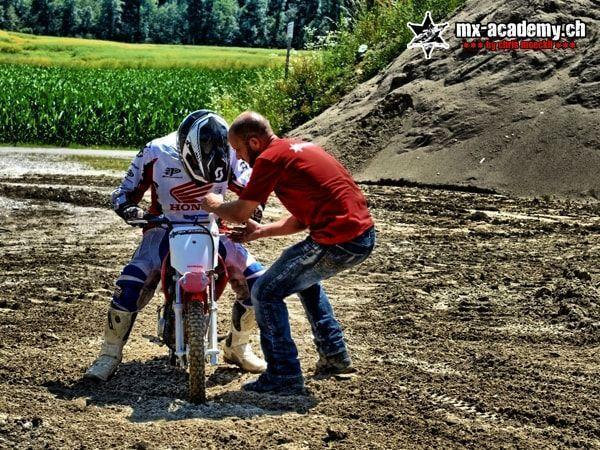 Trainer im roten T-Shirt unterstützt einen Einsteiger auf einer Honda im Schlamm – Motorrad ausprobieren mit Coach
