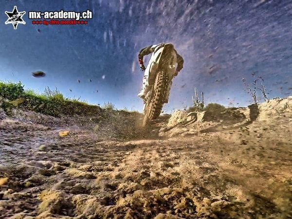 Froschperspektive auf einen Motocross-Fahrer von hinten, die Erde fliegt Richtung Kamera