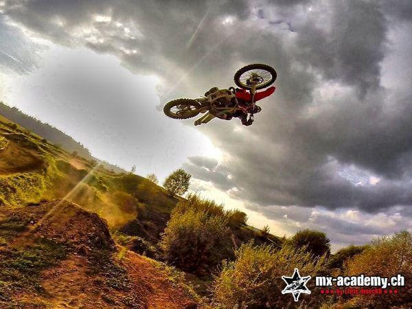 Freestyle Motocross Technik: Fahrer stellt das Motorrad im Sprung quer, dahinter dunkle Wolken