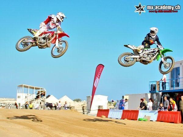 Motorsport Erlebnis: zwei Fahrer springen nebeneinander, darunter Zuschauer und eine Tribüne