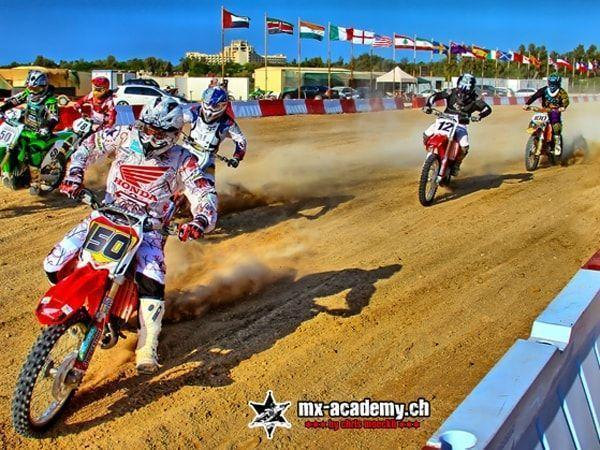 Motorrad Rennsport: Start mehrerer Fahrer auf einer Sandstrecke vor den Fahnen vieler Länder
