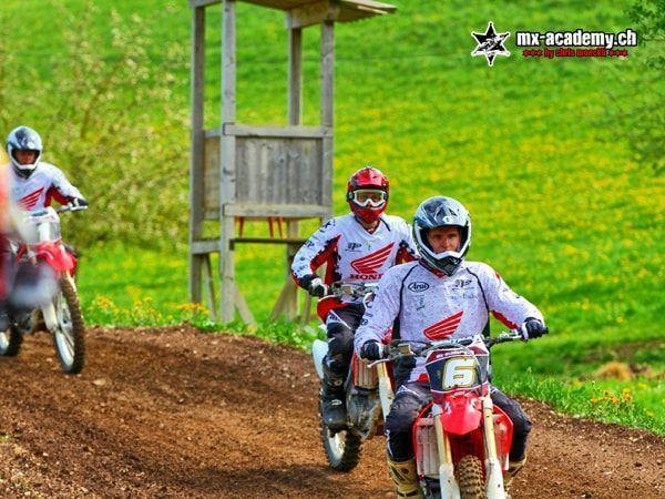Drei Fahrer in Honda-Trikots fahren hintereinander über die Strecke, im Hintergrund ein Hochsitz
