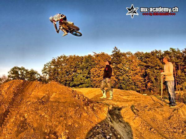 Motocross Fotos: Fahrer im hohen Sprung über einen Erdhügel, oben stehen zwei Zuschauer