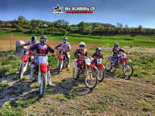 Sechs Fahrer mit ihren Motorrädern auf Schotter vor einer grünen Hügellandschaft – Motocross Kurs Termine