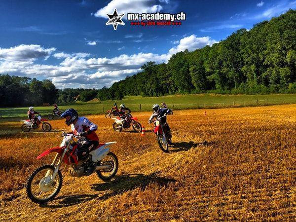 Einsteiger auf roten Honda-Motorrädern im offenen Gelände vor dem Wald – Motocross Einsteigerkurs
