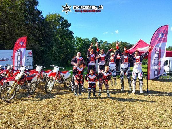 Erwachsene und Kinder springen vor Motorrädern und Zelt jubelnd in die Luft – Motocross Geschenk für jedes Alter