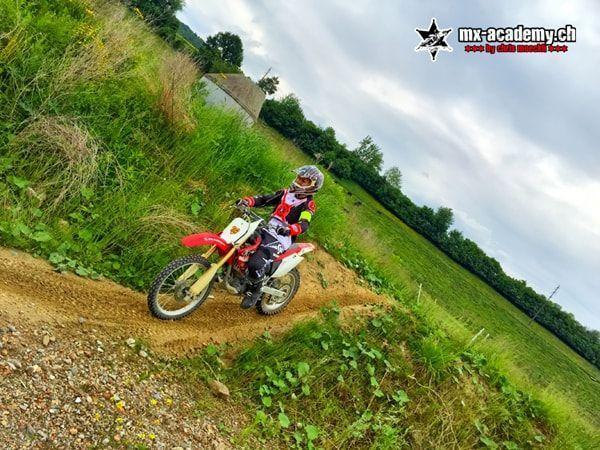 Dirtbike fahren auf einem Erdweg: rote Honda am grünen Hang, aus schrägem Winkel aufgenommen