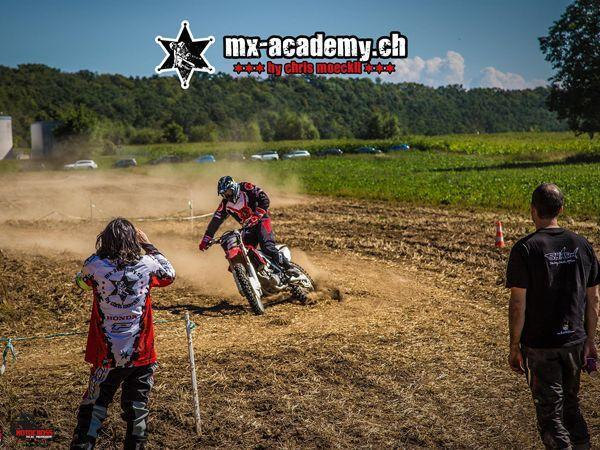 Fahrer wirbelt in der Kurve Staub auf, zwei Personen schauen vom Rand aus zu – Motocross für Anfänger