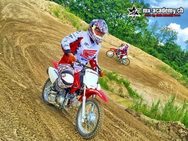 Kind auf einem Honda-Kindermotorrad in einer Sandkurve, ein weiterer Fahrer dahinter – Kurven üben beim Kindercross