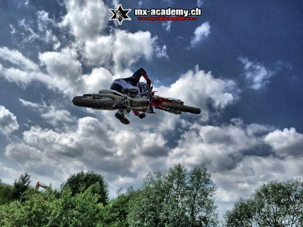 Whip wie im FMX: Fahrer legt das Motorrad im Sprung quer, im Hintergrund ein Wolkenhimmel