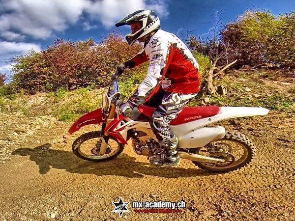 Stehend durch die Kurve auf der roten Honda, im Hintergrund rotbraune Büsche – Dirt Bike Technik