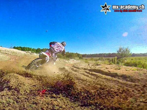 Drift in der Kurve: Unter dem Dirt Bike fliegen Erdbrocken weg, darüber ein blauer Himmel