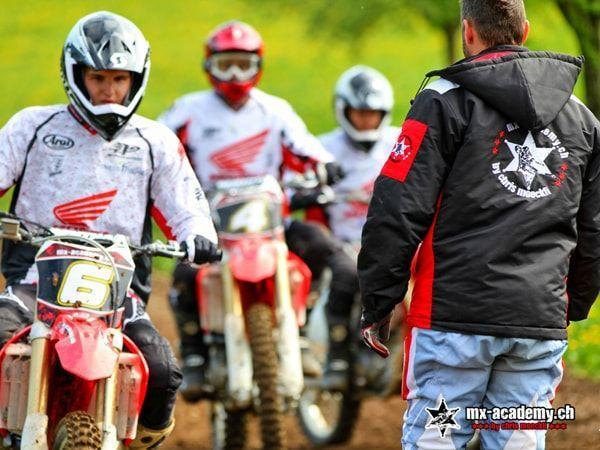 Drei Fahrer in Honda-Trikots hören dem Trainer in MX-Academy-Jacke zu – Theorie im Motocross Anfängerkurs