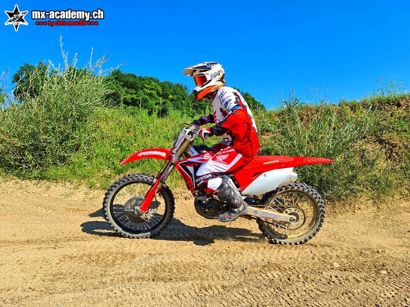 Motocross-Fahrer auf roter Honda CRF auf der Sandstrecke, blauer Himmel – Fahrwerk Service für Offroad