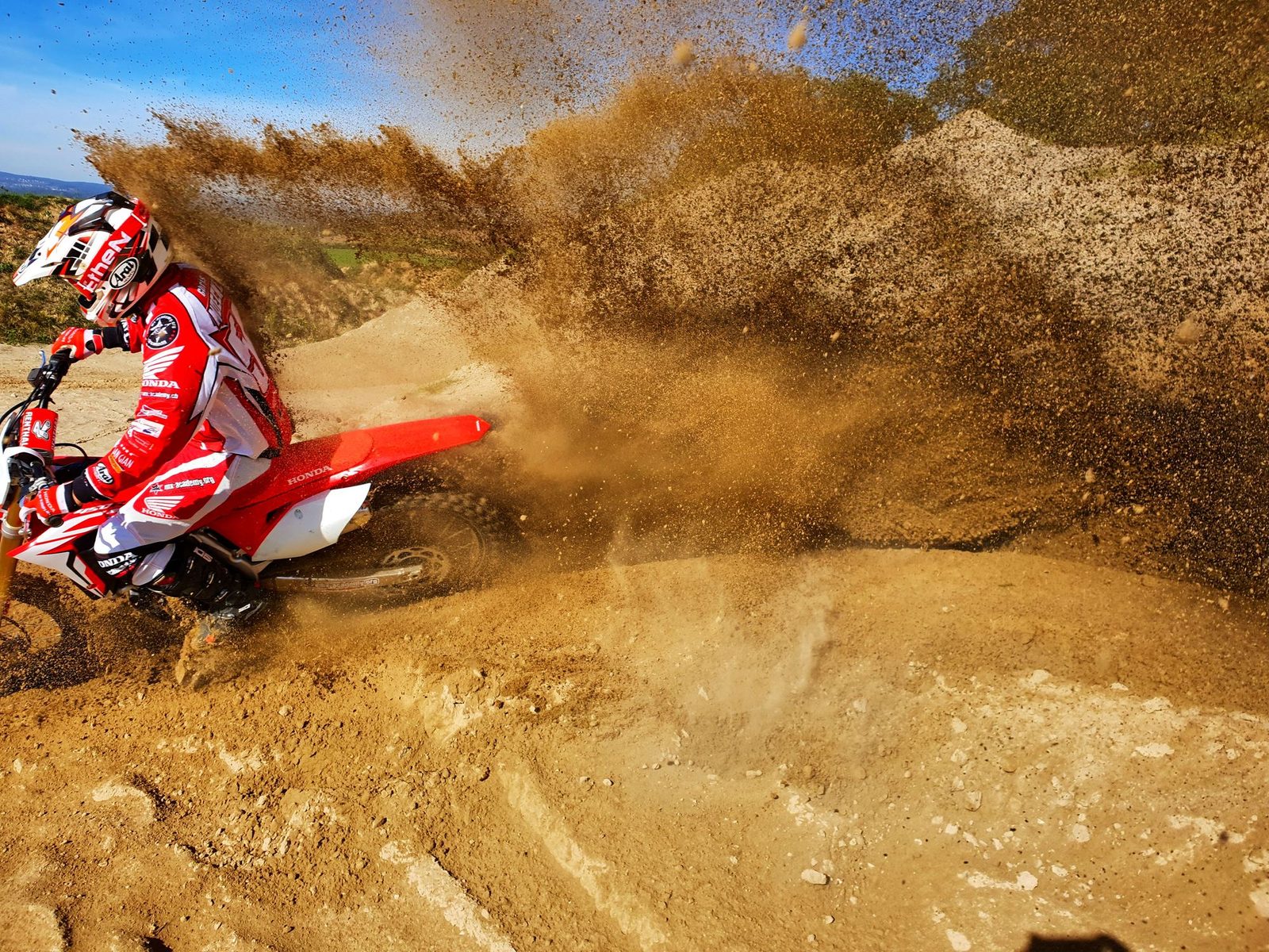 Motocross fahren ab Deutschland: Fahrer mit Sandfontäne in der Kurve