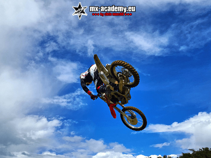 Motocross Verein in Aktion: Fahrer springt vor blauem Himmel über die Strecke