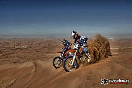 Motocross Dubai: zwei Fahrer in den Sanddünen, hinter ihnen fliegt eine Sandfontäne hoch